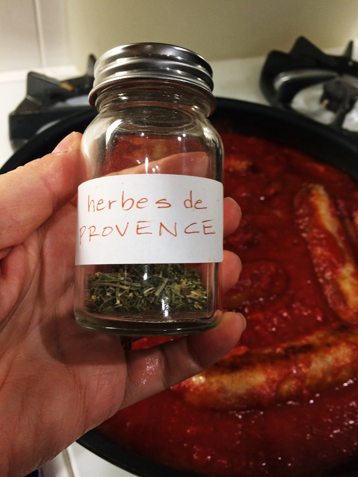A bottle of herbs de provence by pan of ragu
