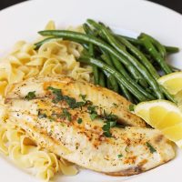 plate of fish, buttered noodles, green beans, and lemon slices