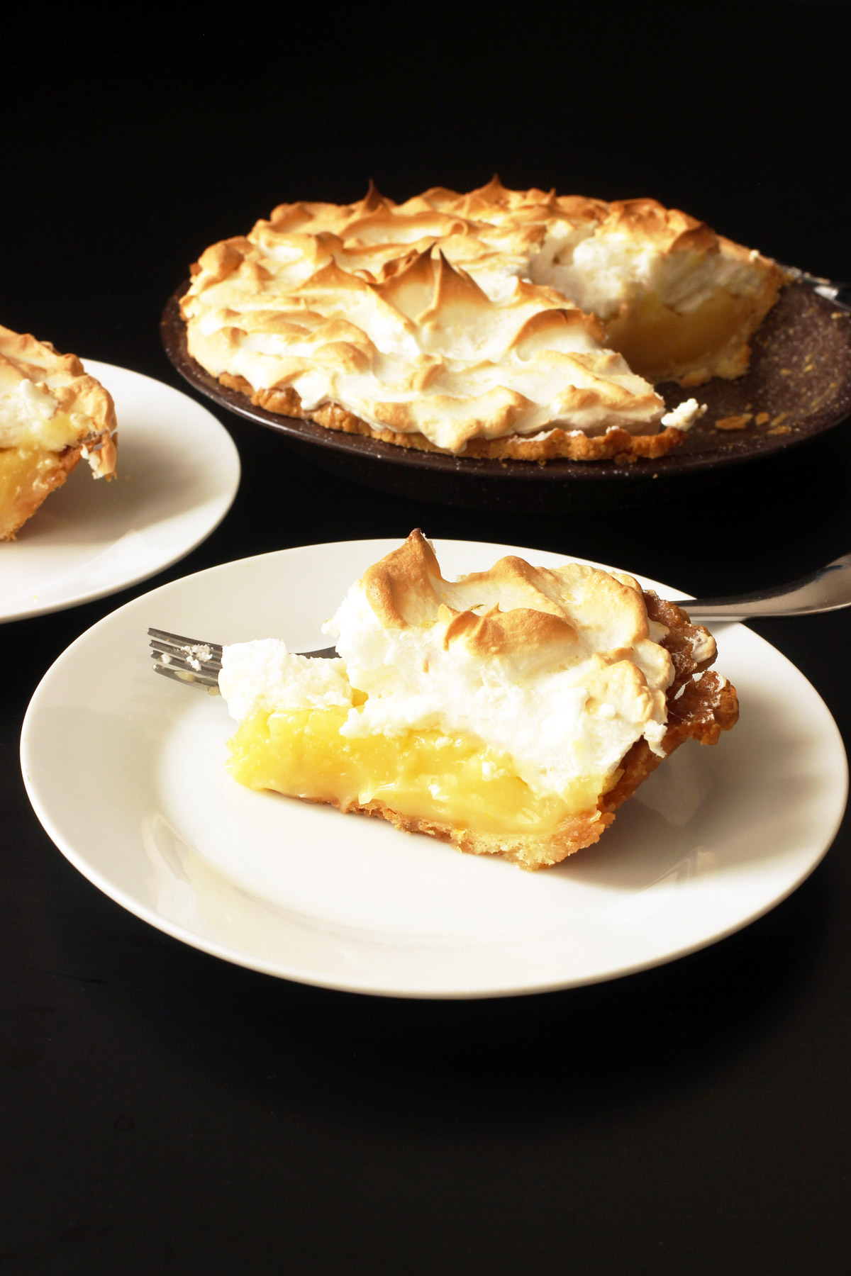 lemon pie dished on plates next to pie plate on table.