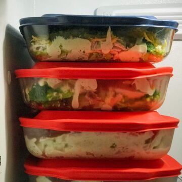 stack of pyrex dishes with lids filled with casseroles in the freezer.