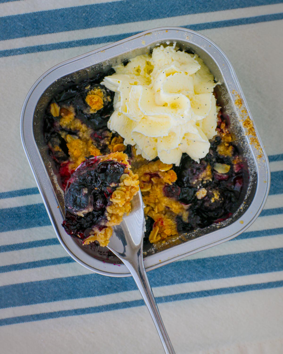 blue and white striped cloth with mini blueberry crumble on top, with a spoon.