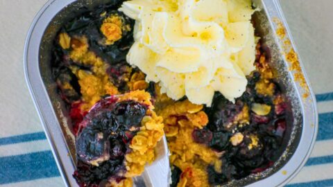 overhead shot of blueberry crumble with a spoon scooping out a bite, whipped cream on top.