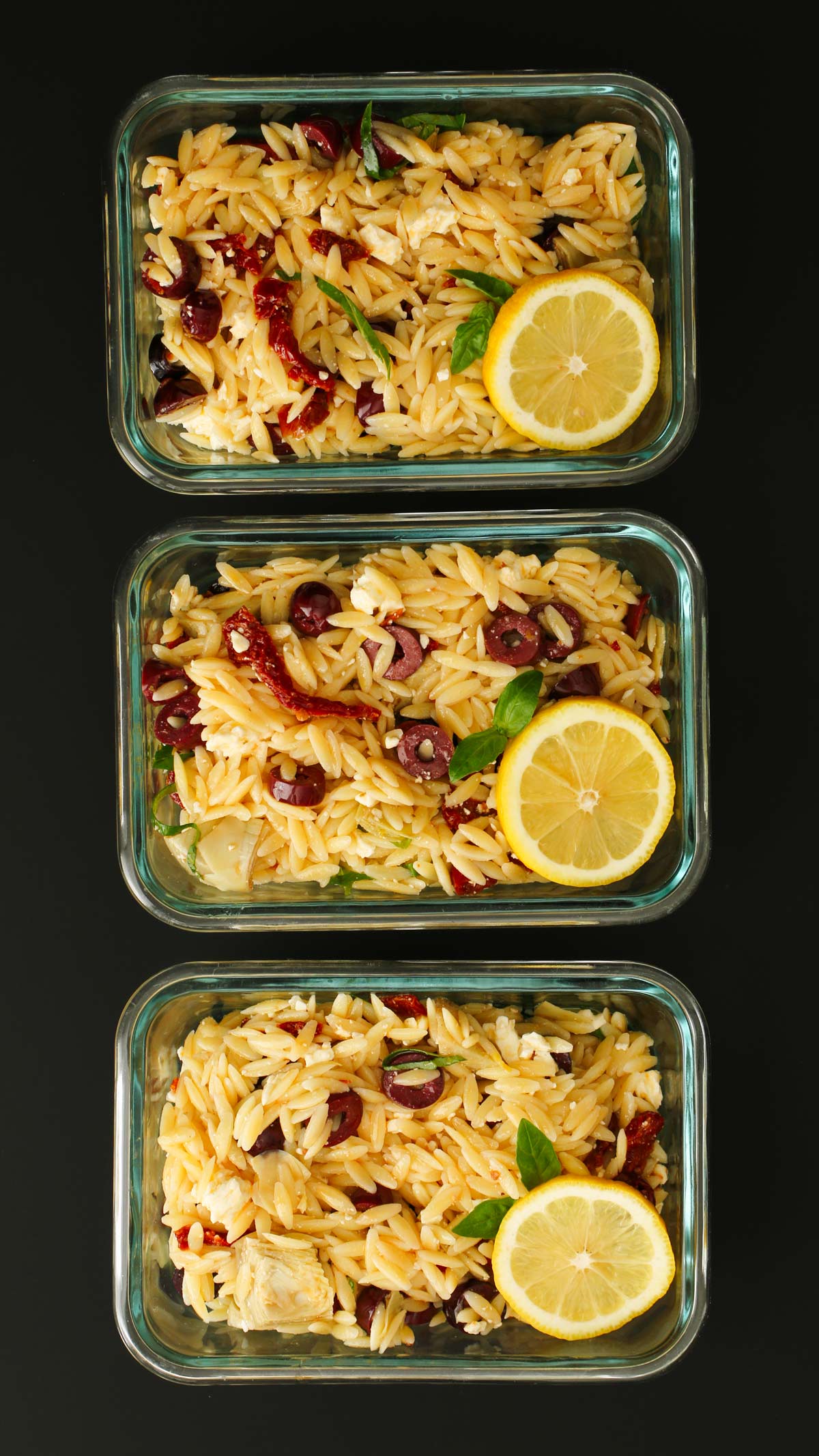 glass meal prep dishes filled with orzo salad and garnished with lemon.
