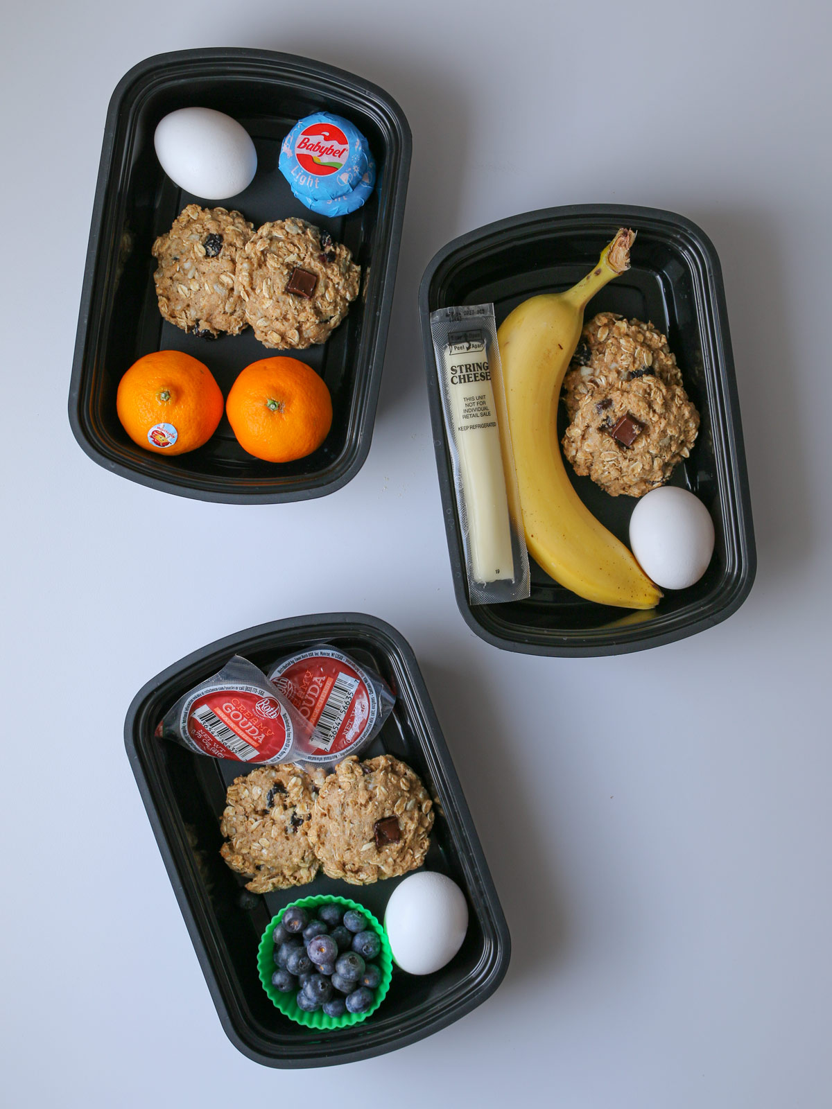 meal prep boxes packed with fruit, protein cookies, eggs, and cheese.
