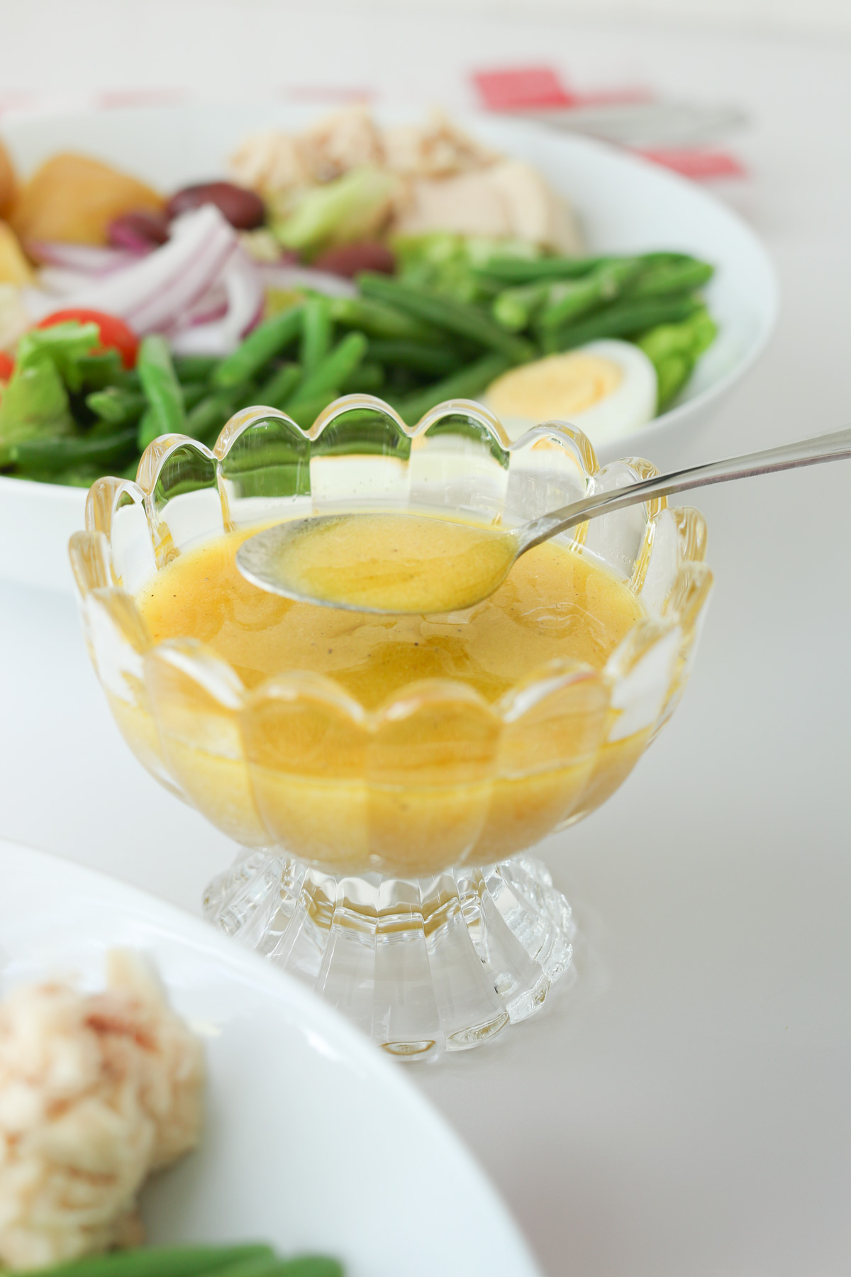 spoon dishing up dijon vinaigrette from decorative glass bowl.