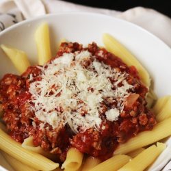 A bowl of pasta with meat sauce with cheese