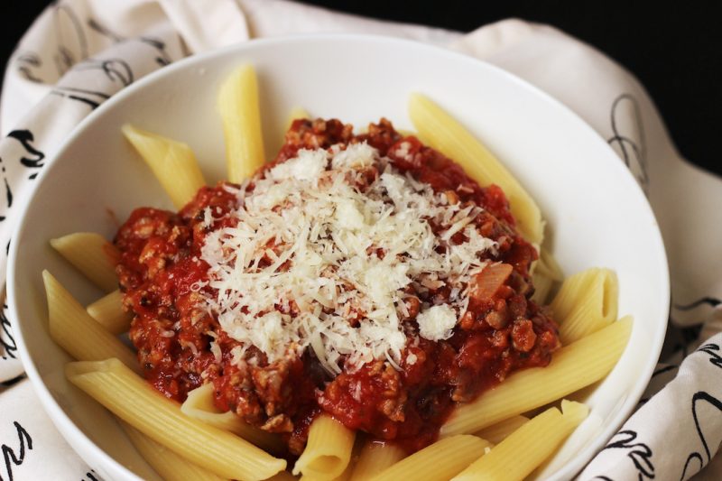 A bowl of pasta with meat sauce with cheese