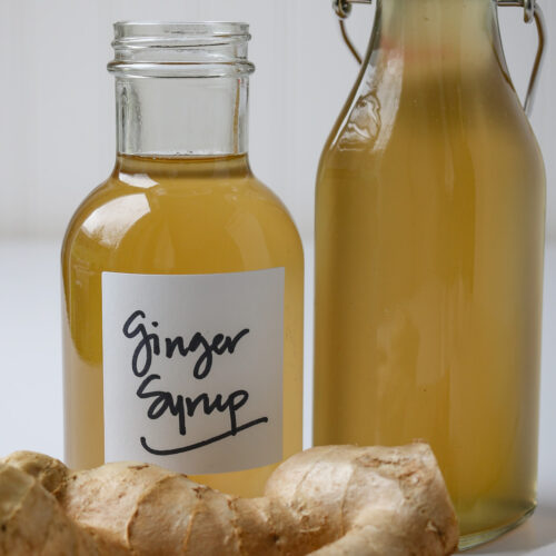 ginger syrup bottles next to hunk of ginger root.