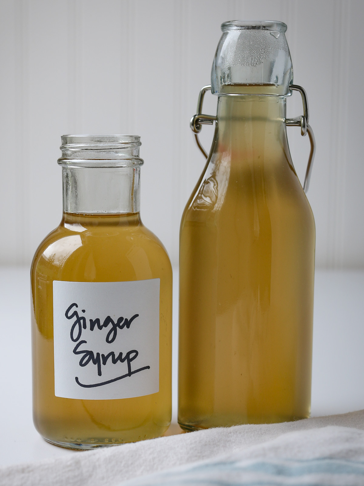 two bottles of ginger syrup on a table with a blue striped cloth.