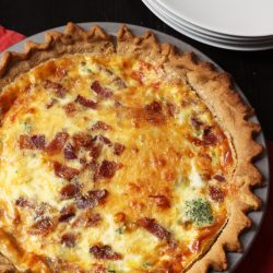 bacon quiche in pie plate with stack of plates and red napkin