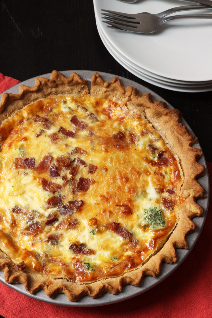 bacon quiche in pie plate with stack of plates and red napkin