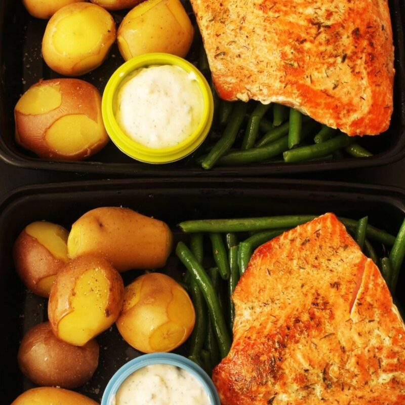 black meal prep boxes with fish, green beans, potatoes, and tartar sauce.