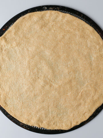 plain round of whole wheat pizza dough on a screen.