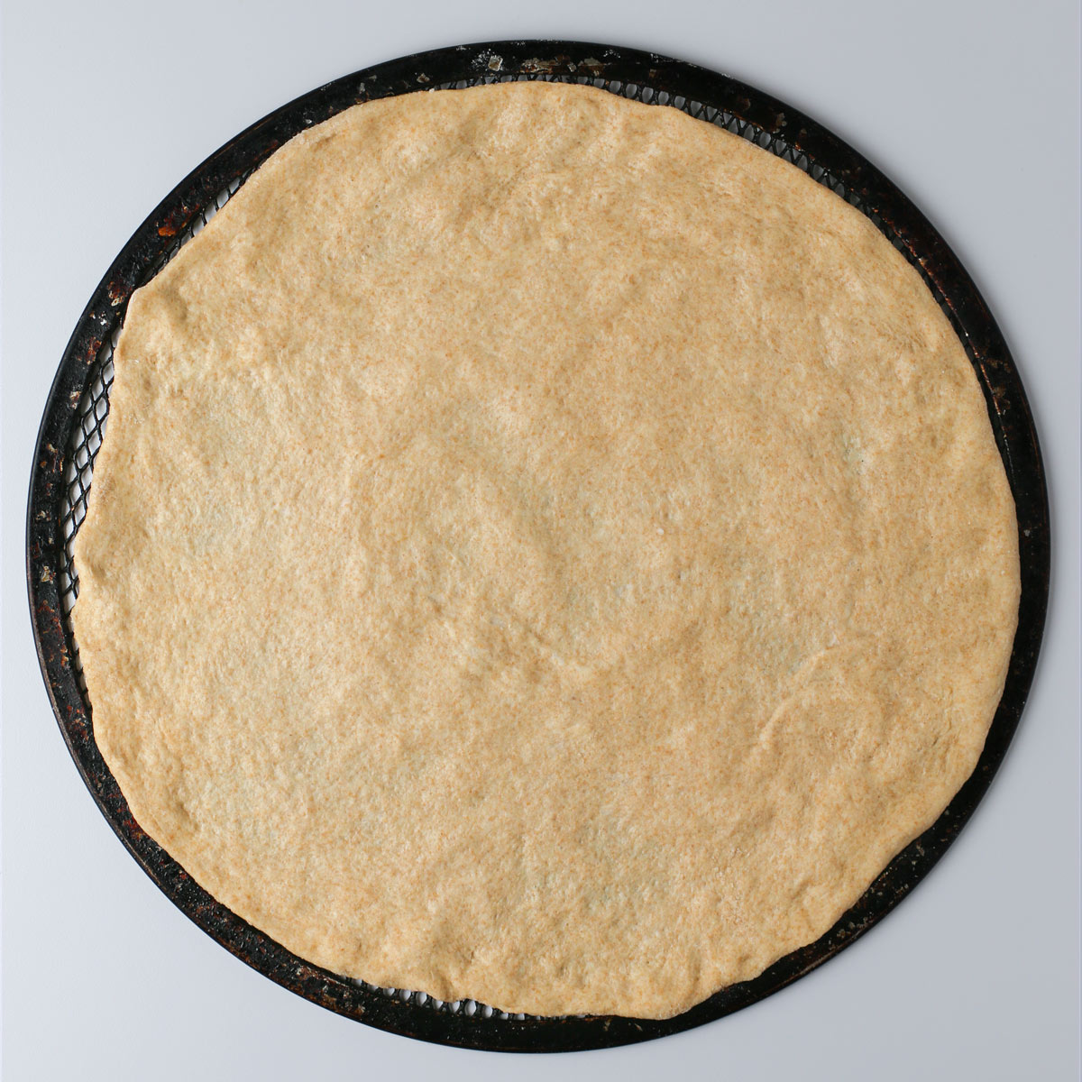 plain round of whole wheat pizza dough on a screen.