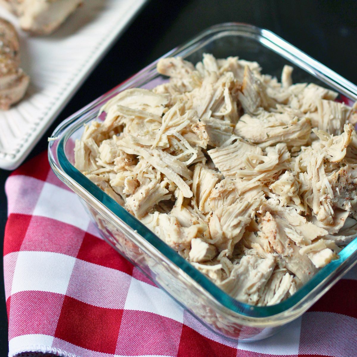 shredded chicken in square glass dish on red check cloth.
