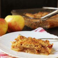 slice of slab apple pie on plate next to apples