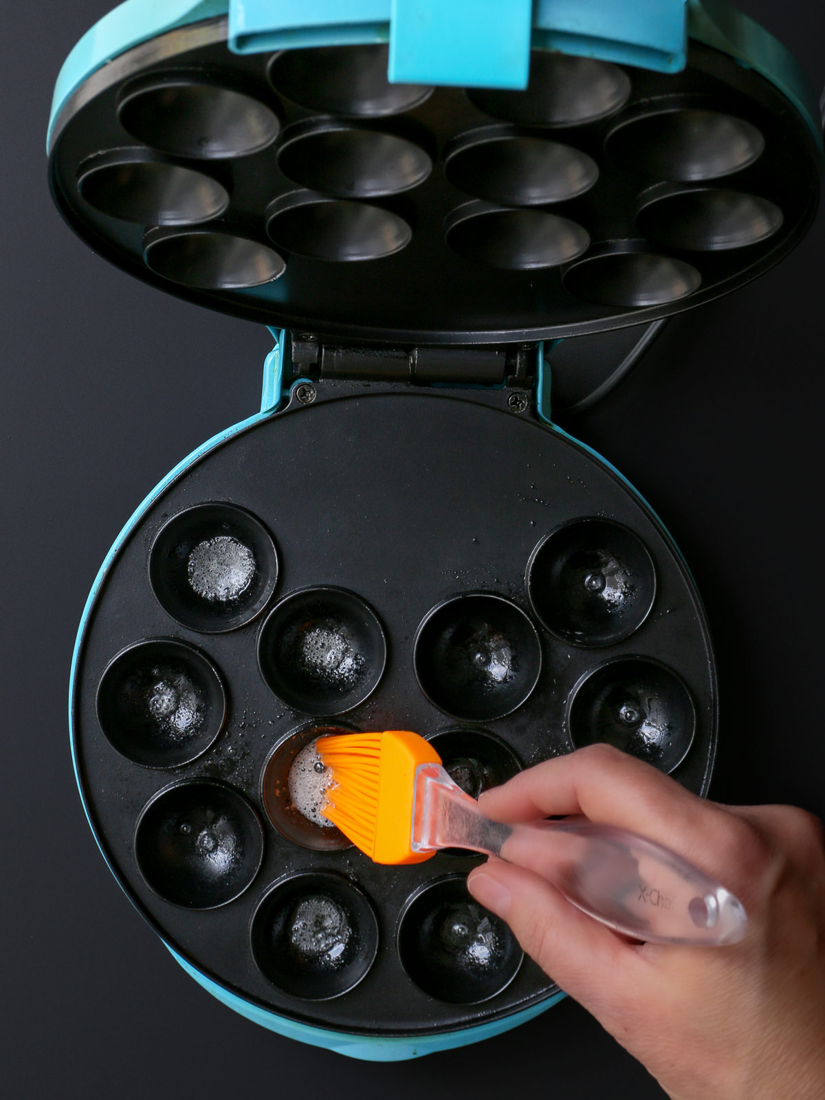 buttering cups of cake pop maker with brush.