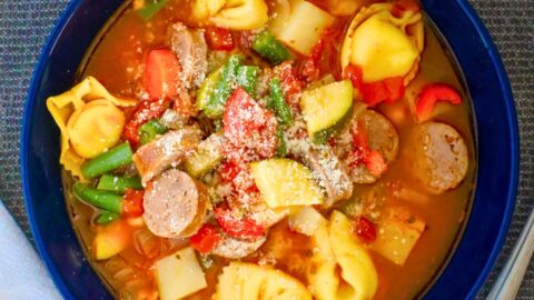 overhead shot of tortellini minestrone in a deep blue bowl.