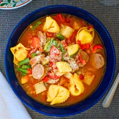 overhead shot of tortellini minestrone in a deep blue bowl.