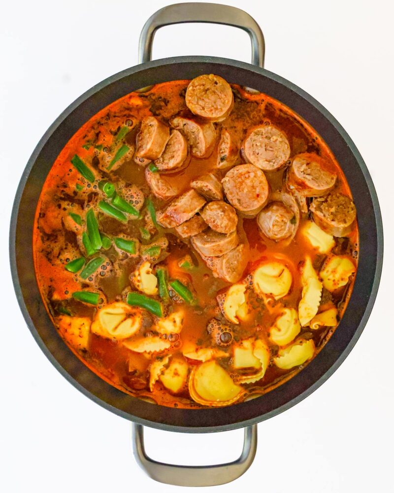 adding sausage, pasta, and beans to the pot.