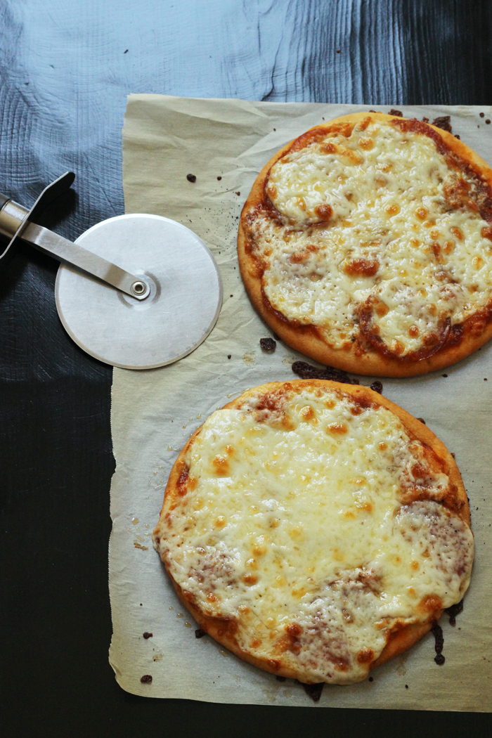 two cheese pita pizzas on parchment paper with a pizza wheel