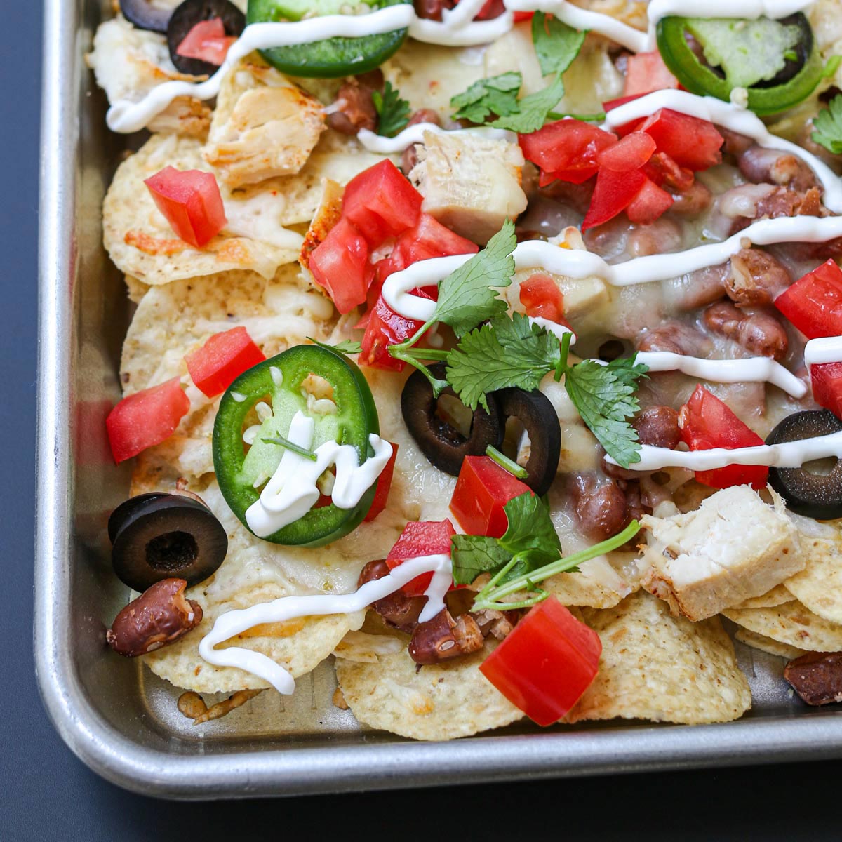 close up of corner of sheetpan filled with nachos topped with cilantro and jalapeno slices.