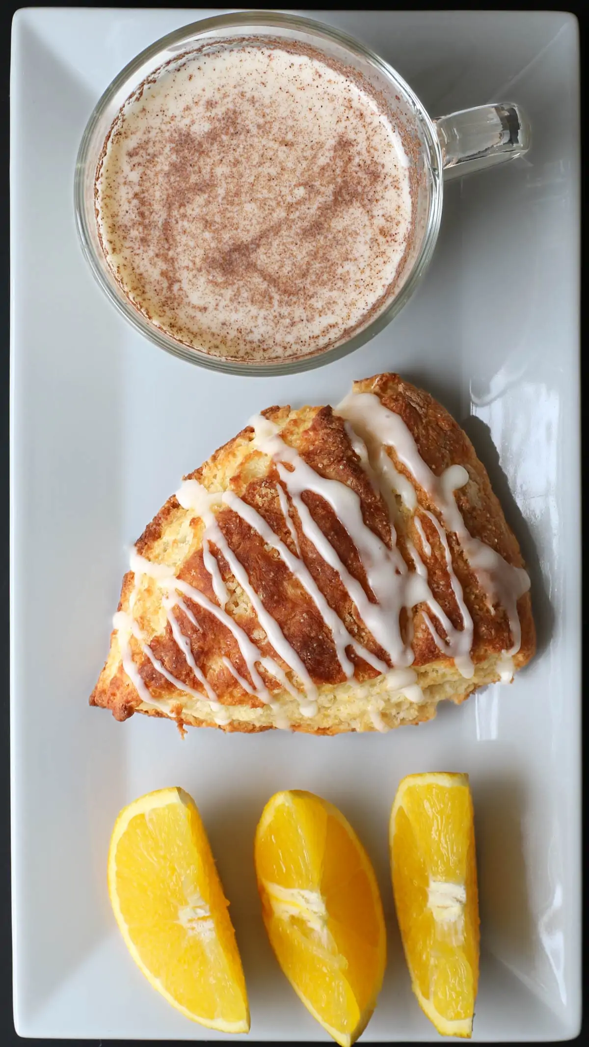 orange scone on a white platter with orange slices and a cup of chai.