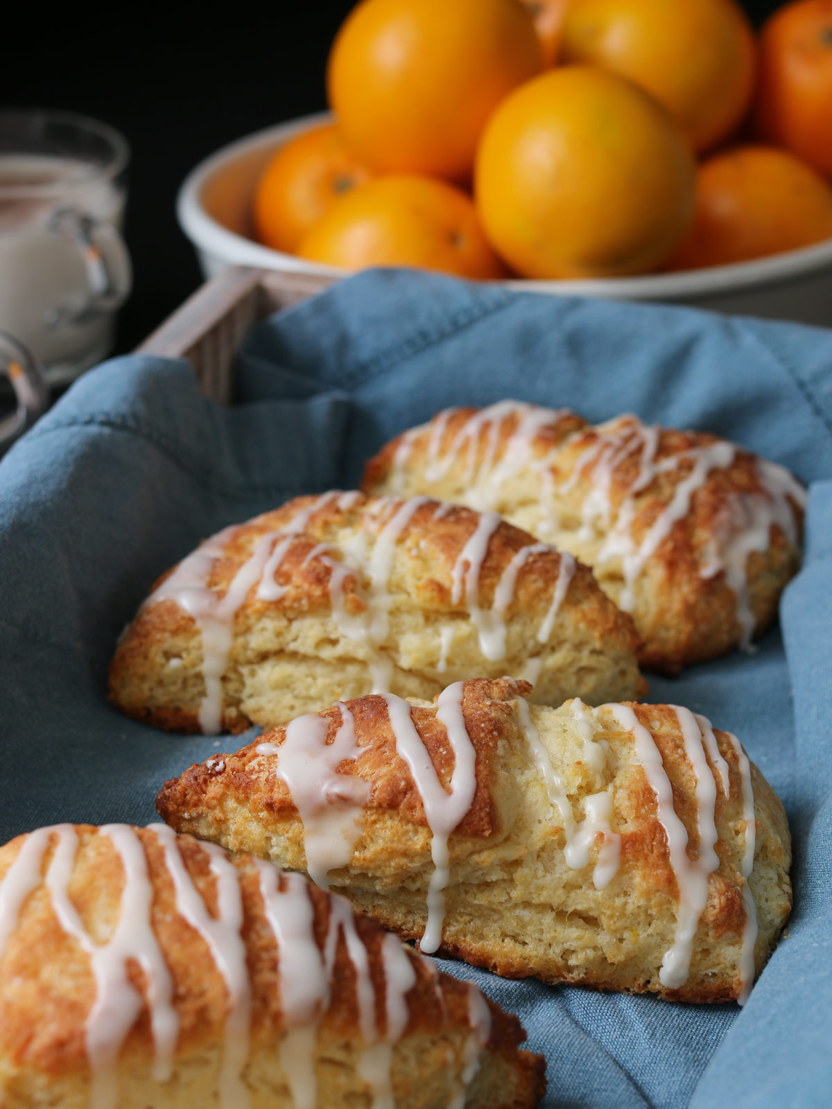 orange scones in a tray lined with a blue cloth, in front of a bowl of oranges.
