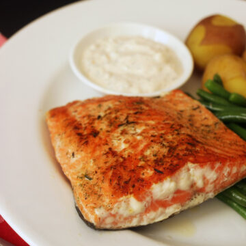 cooked salmon on dinner plate with dish of tartar sauce
