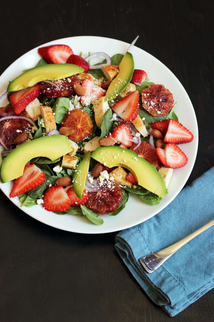 spinach salad topped with fruit and sliced avocado