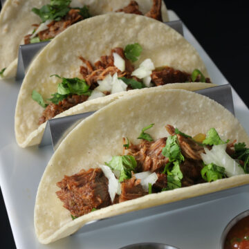 shredded beef tacos in metal holder on white plate.
