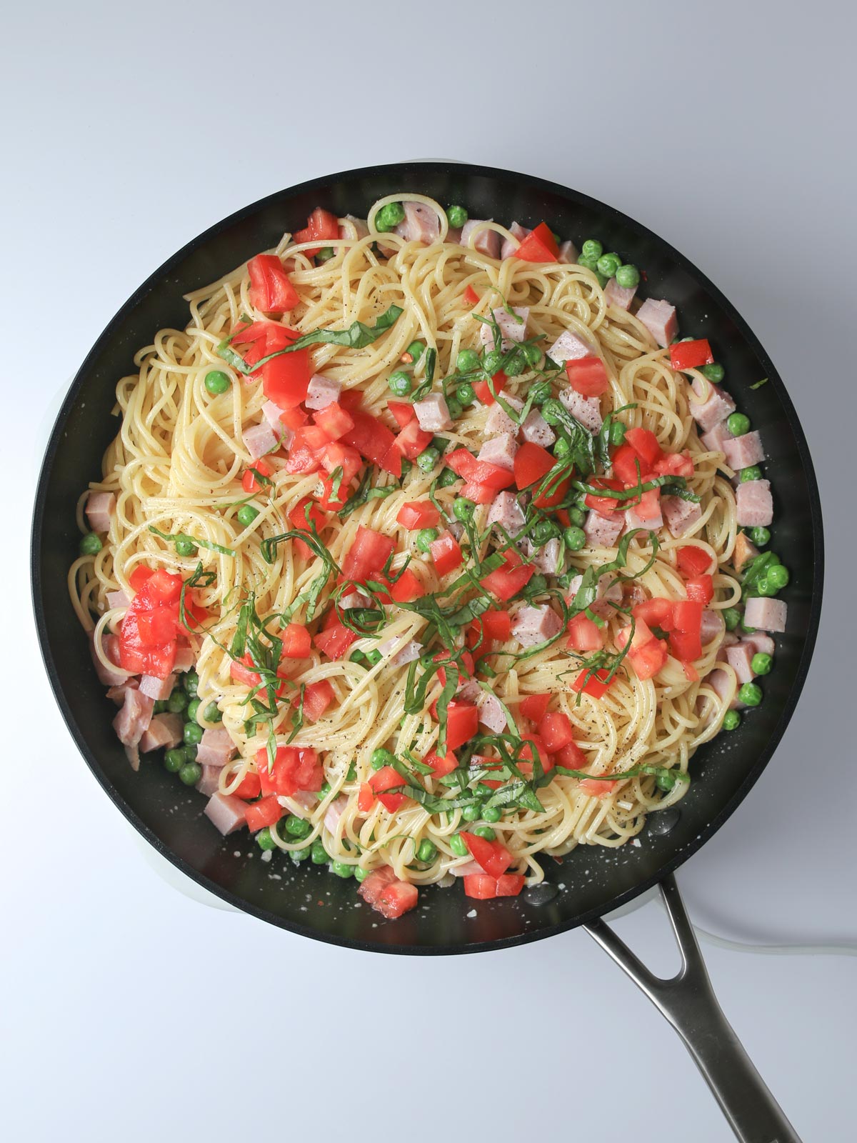 the finished pasta in the skillet with tomatoes and fresh basil.