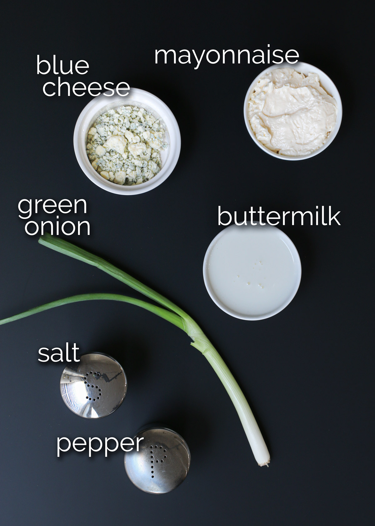 ingredients needed for blue cheese dressing laid out on a black table.