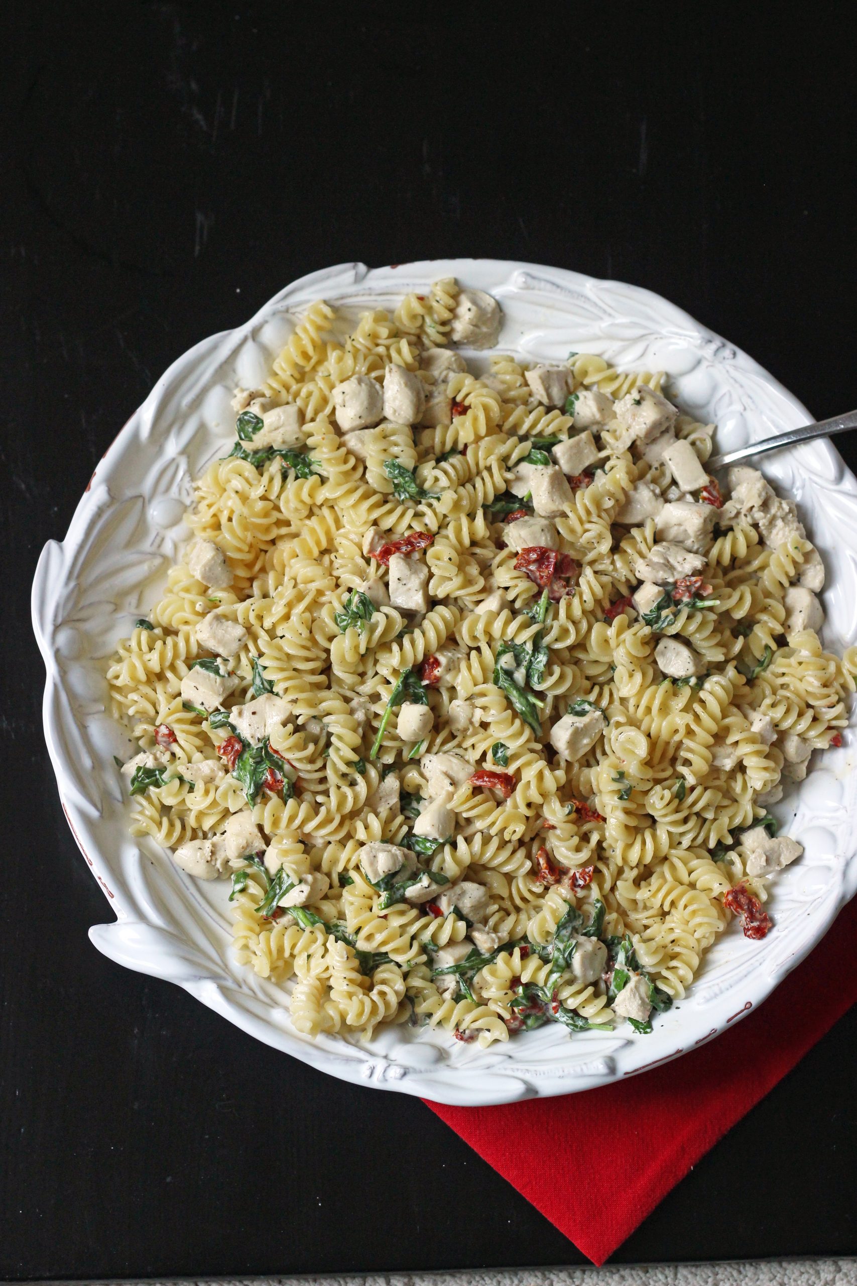 creamy chicken pasta in large white bowl with red cloth on black table.