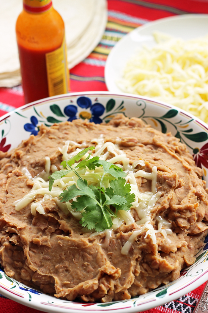 bowl of refried beans with bowl of cheese and bottle of hot sauce