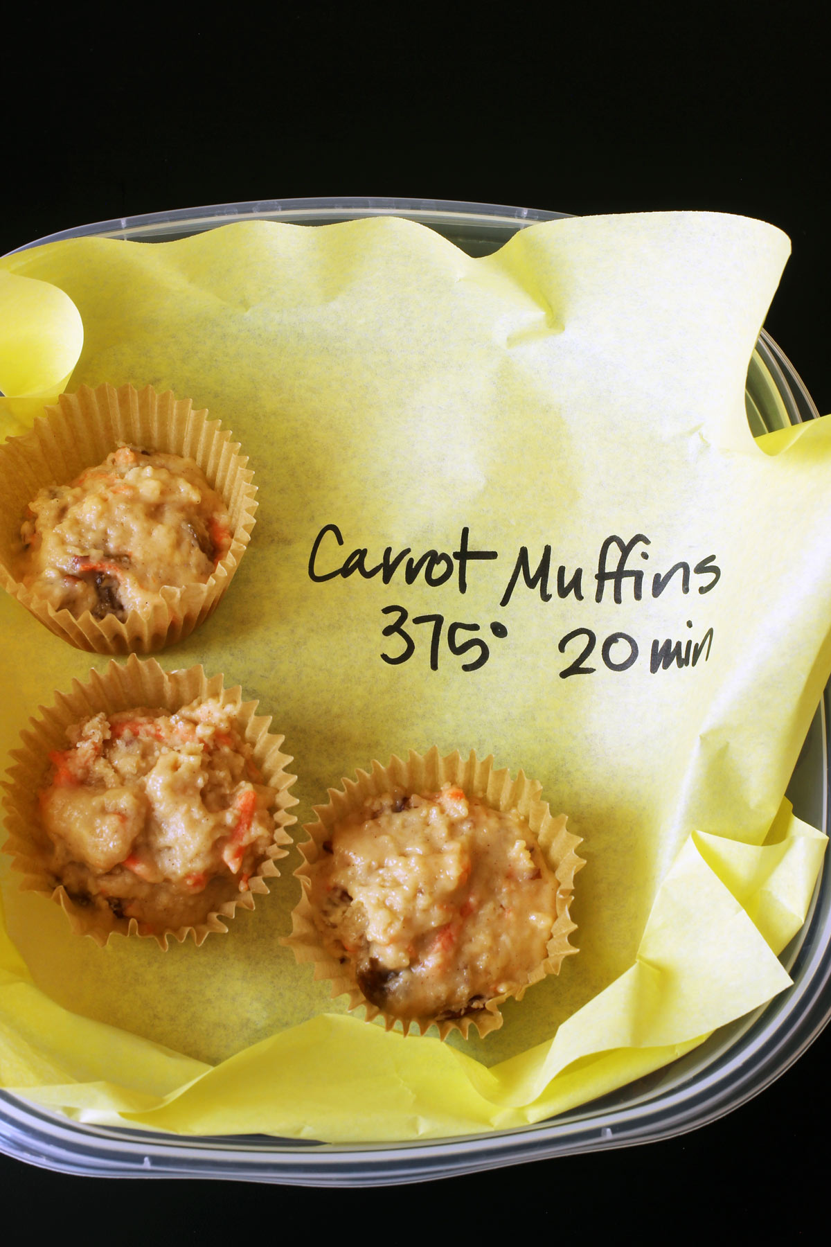 frozen muffins in papers in a freezer-safe container with a deli wrap marked with baking instructions.