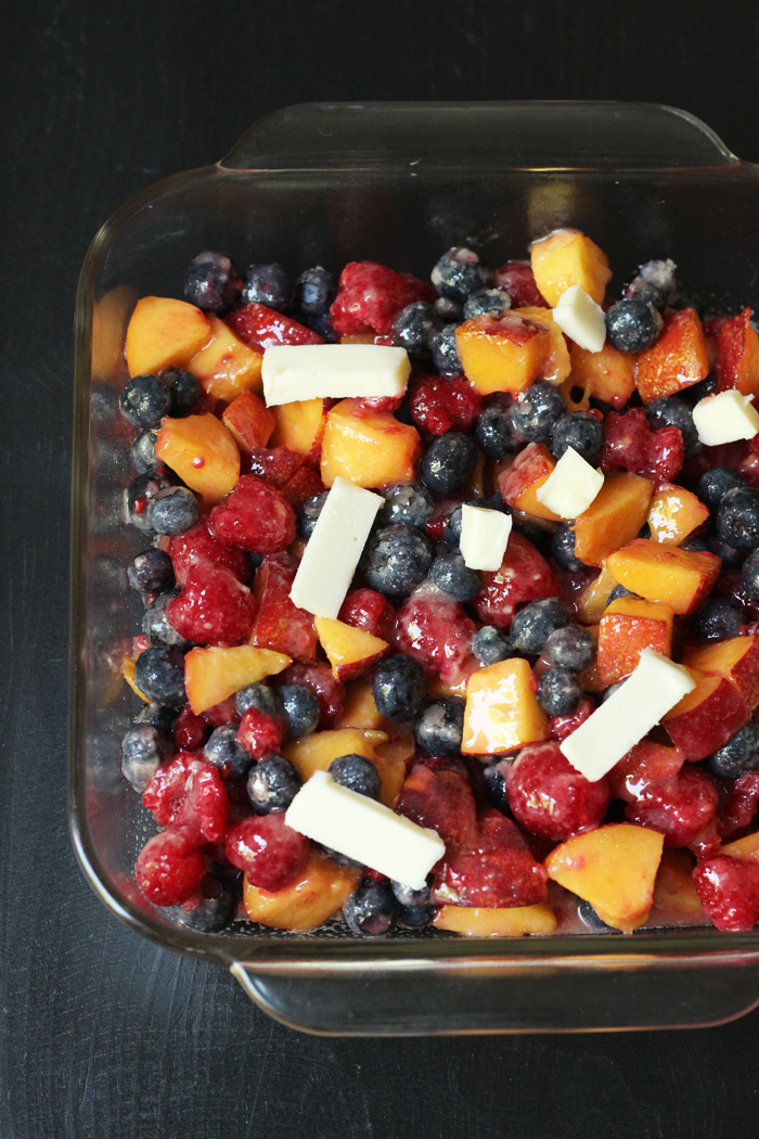 fruit cobbler filling in a glass dish dotted with butter