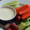 A cup of ranch on plate of veggies
