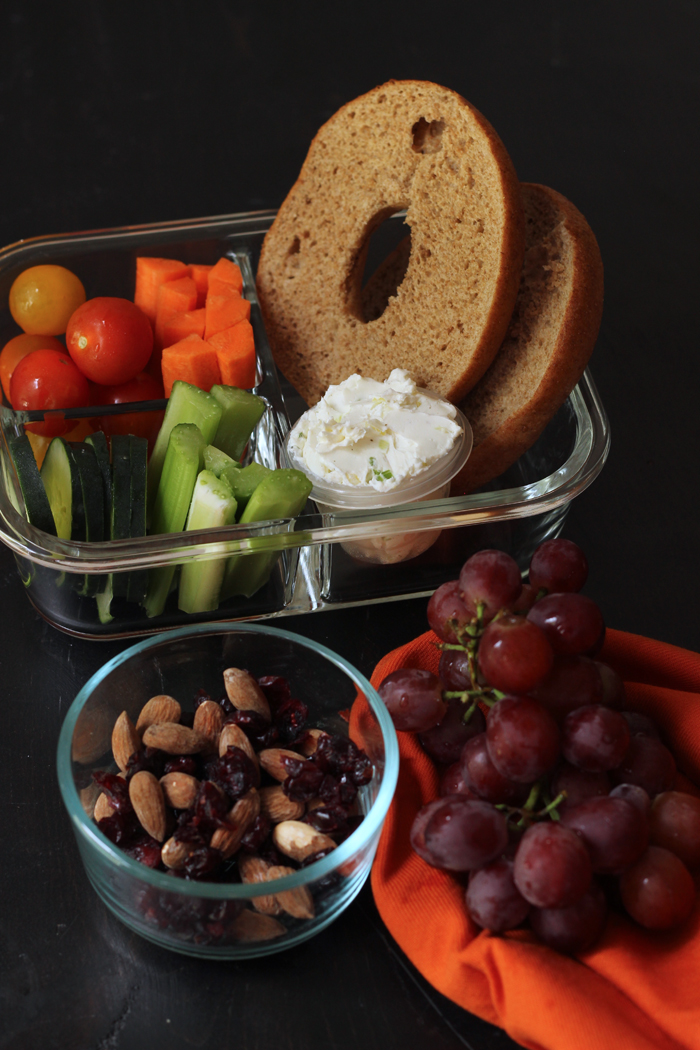 bagel with veggies in a container with a grapes and nuts