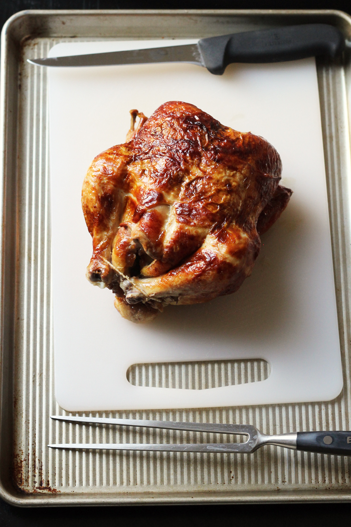 un pollo entero sobre una tabla de cortar con un cuchillo de deshuesar y un tenedor de cocina