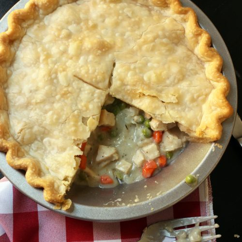 pot pie with slices removed next to fork and red checked cloth