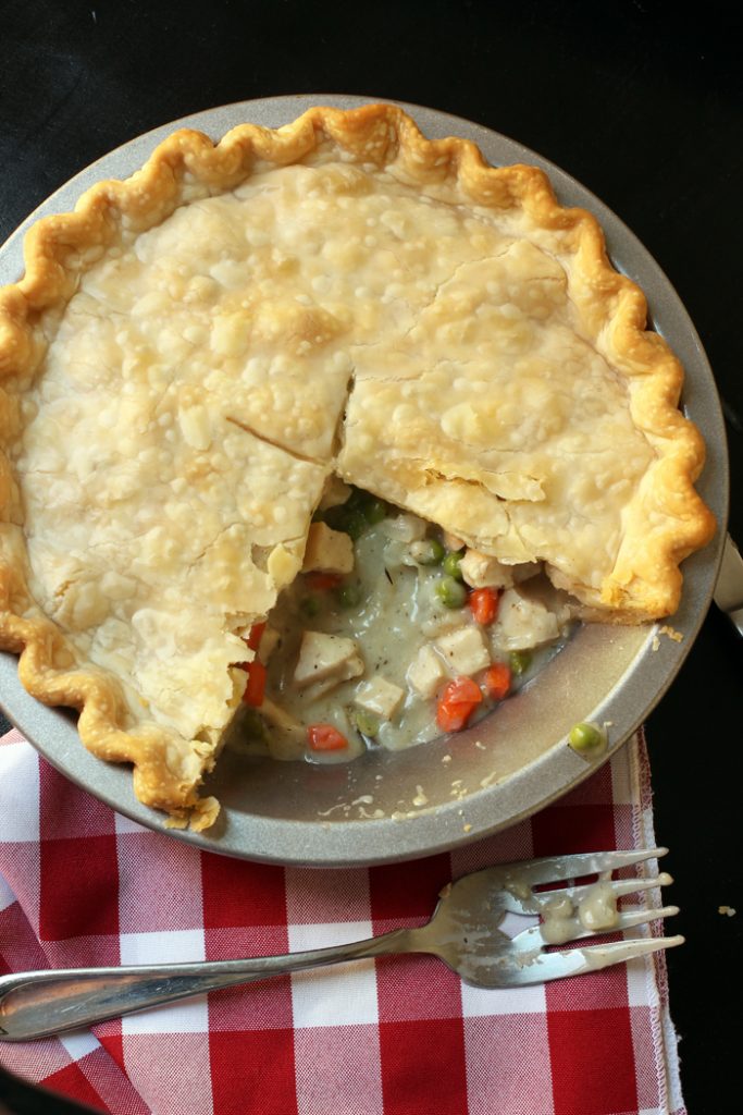 pot pie with slices removed next to fork and red checked cloth