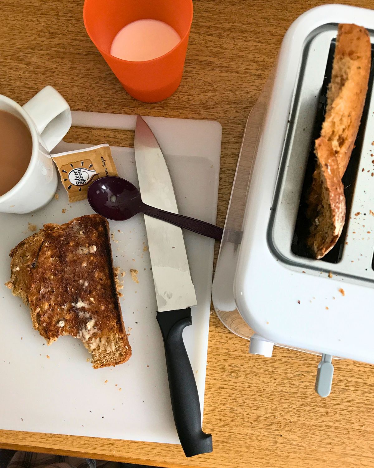 toaster on uk hotel counter with cutting board and knife and cups of milk and tea.