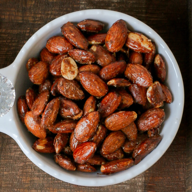 candied almonds in a white bowl on a wood surface.