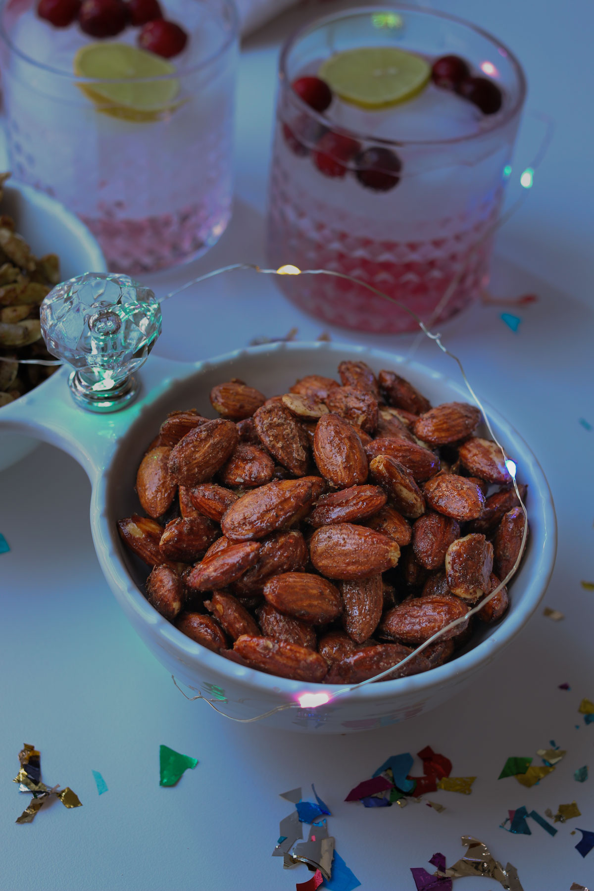 bowl of candied almonds on table with cocktails and confetti.