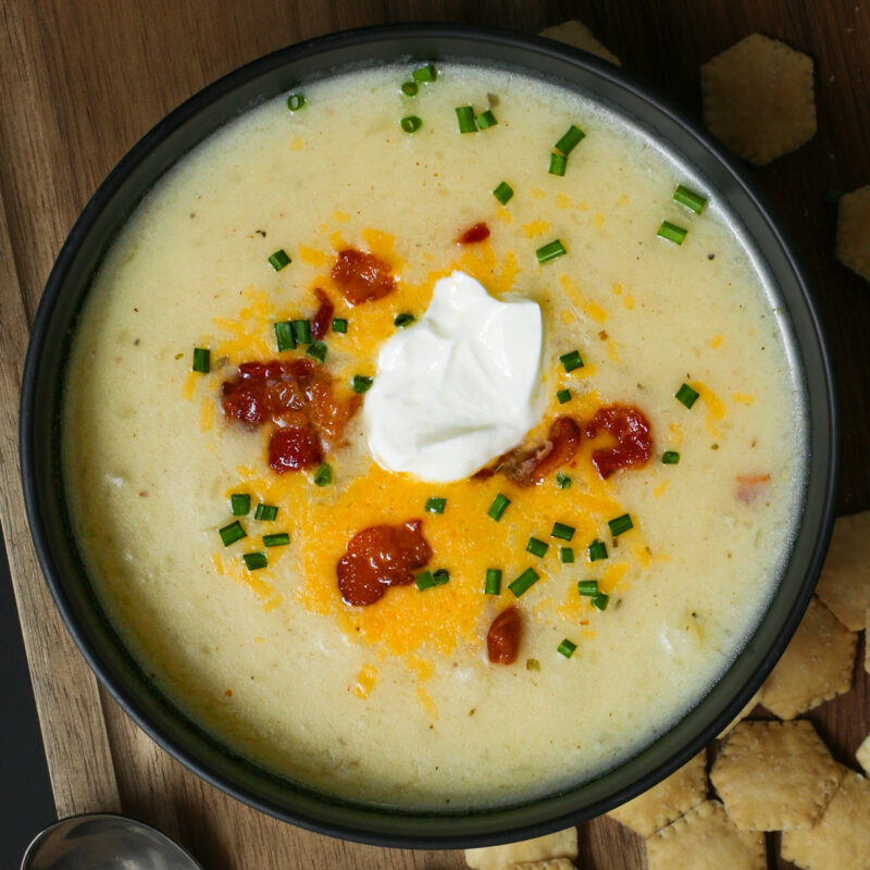 overhead shot of potato soup in black bowl on wooden board.