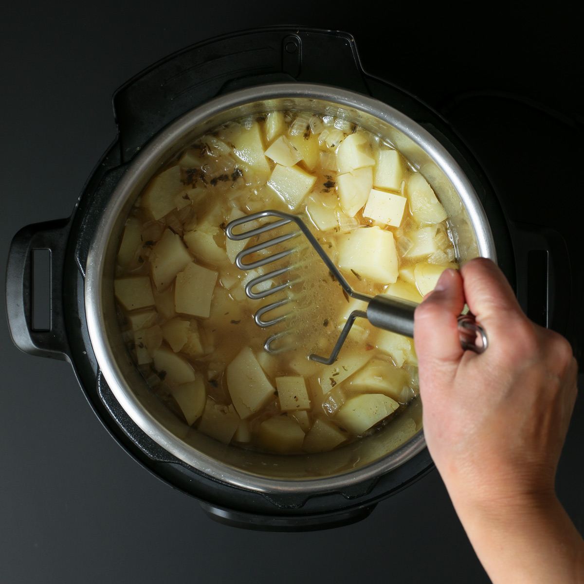 mashing potatoes with masher in pot.