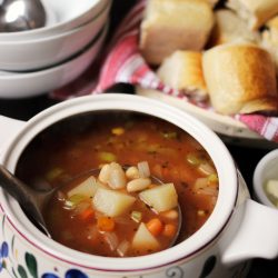 tureen of spicy vegetable soup with basket of rolls