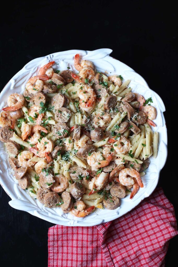 overhead shot of large dish of cajun chicken pasta with sausage on black table with red cloth.