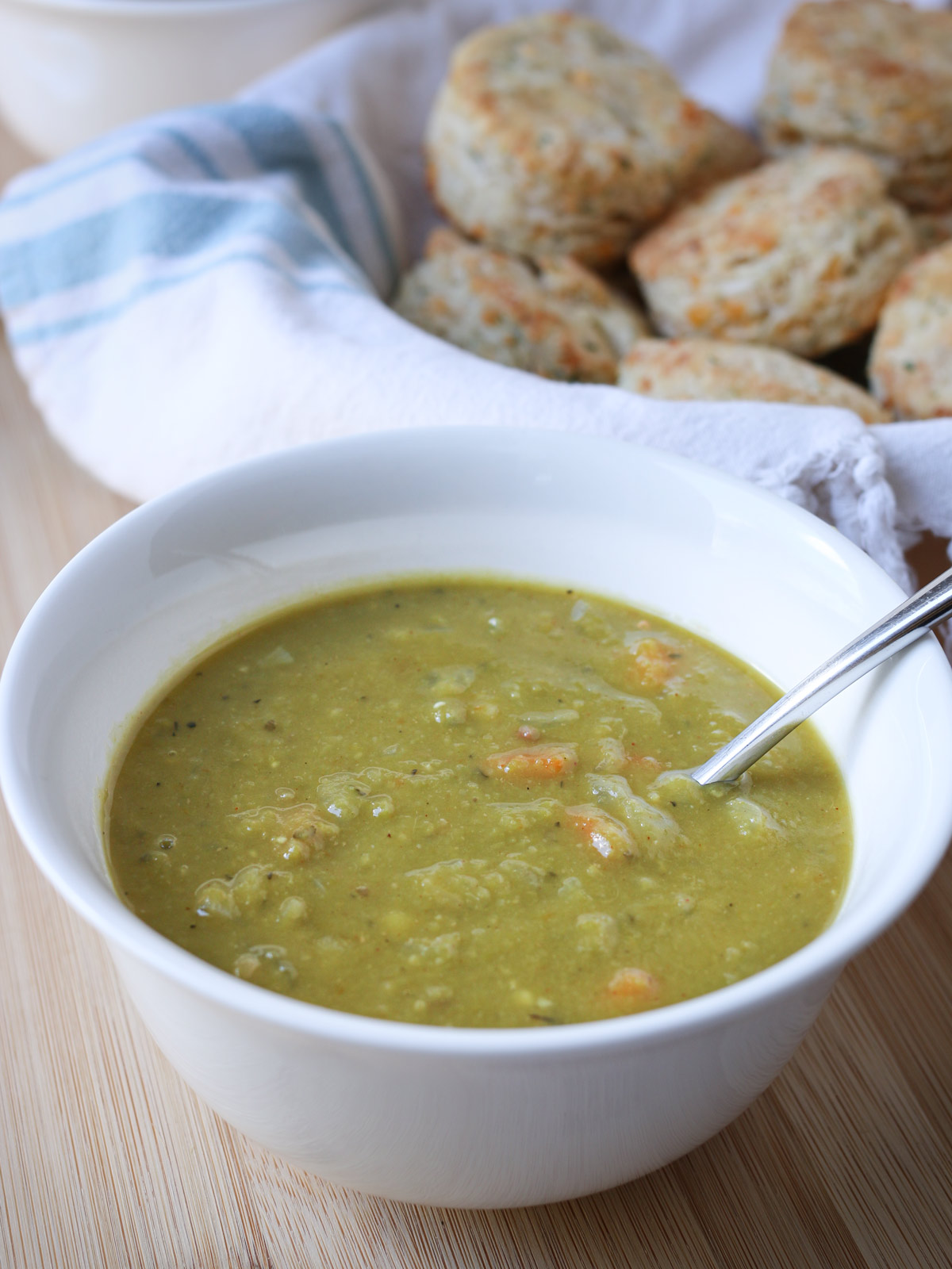 bowl of split pea soup on wood table, with basket of cheese biscuits in background.